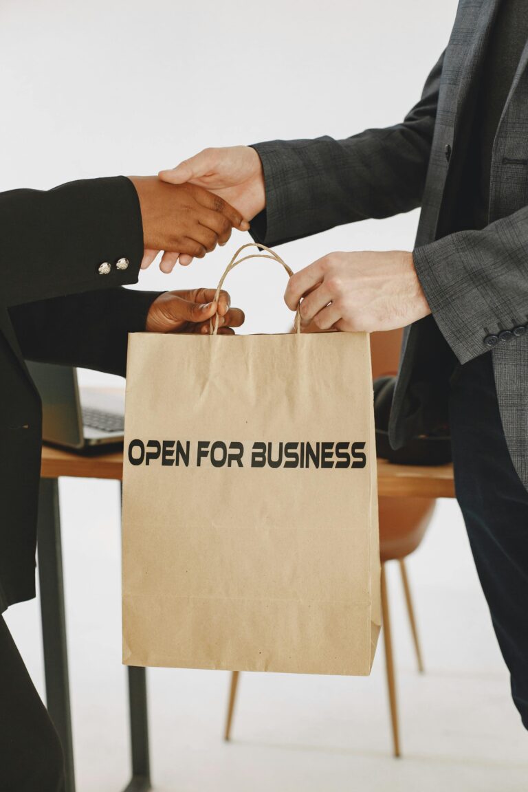 Handshake between two businessmen exchanging an 'Open for Business' bag, symbolizing a successful deal.